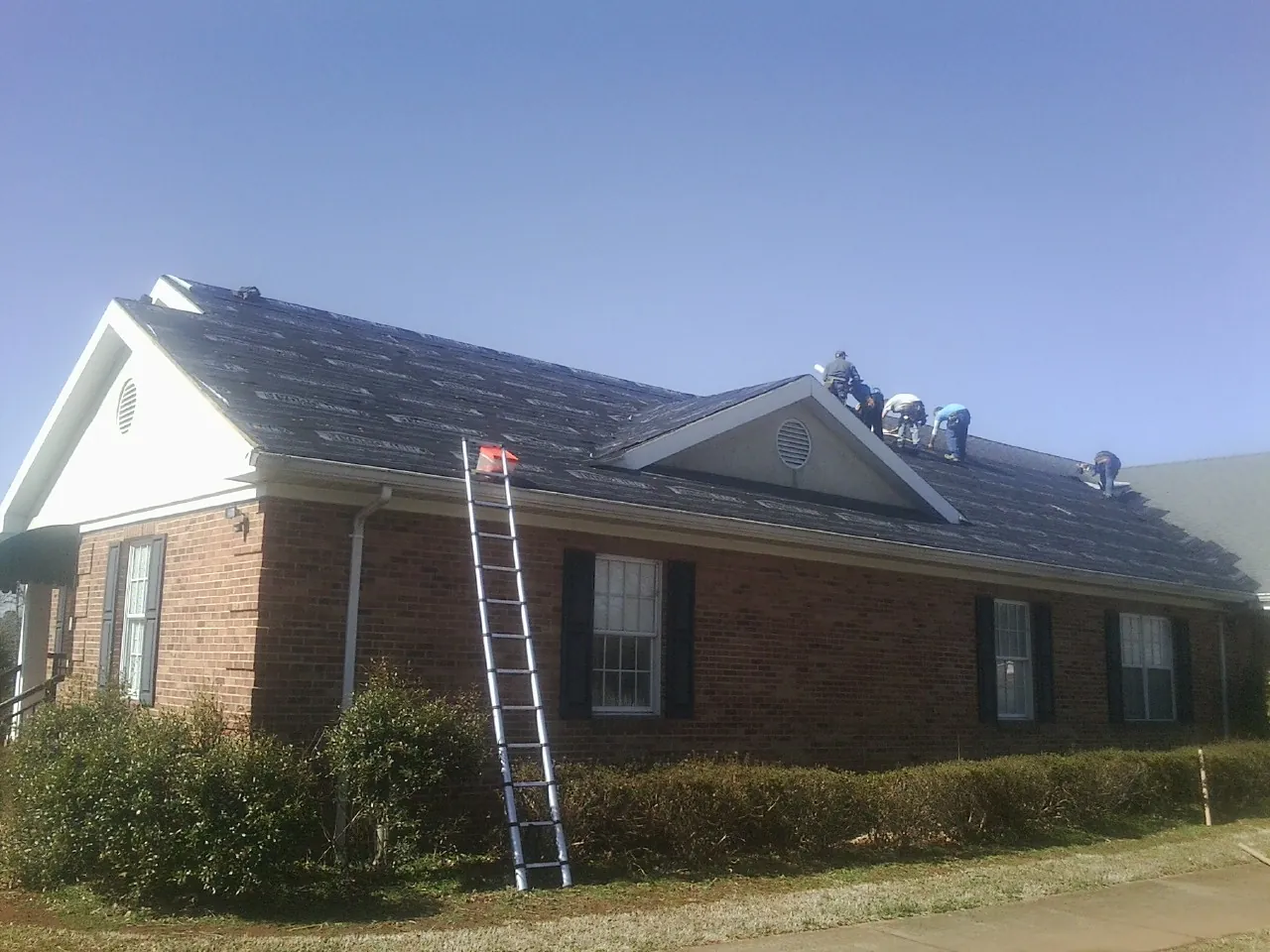 Crew tearing shingles off a brick ranch roof with a ladder set — Emergency Roof Repair work by our crew in Williams