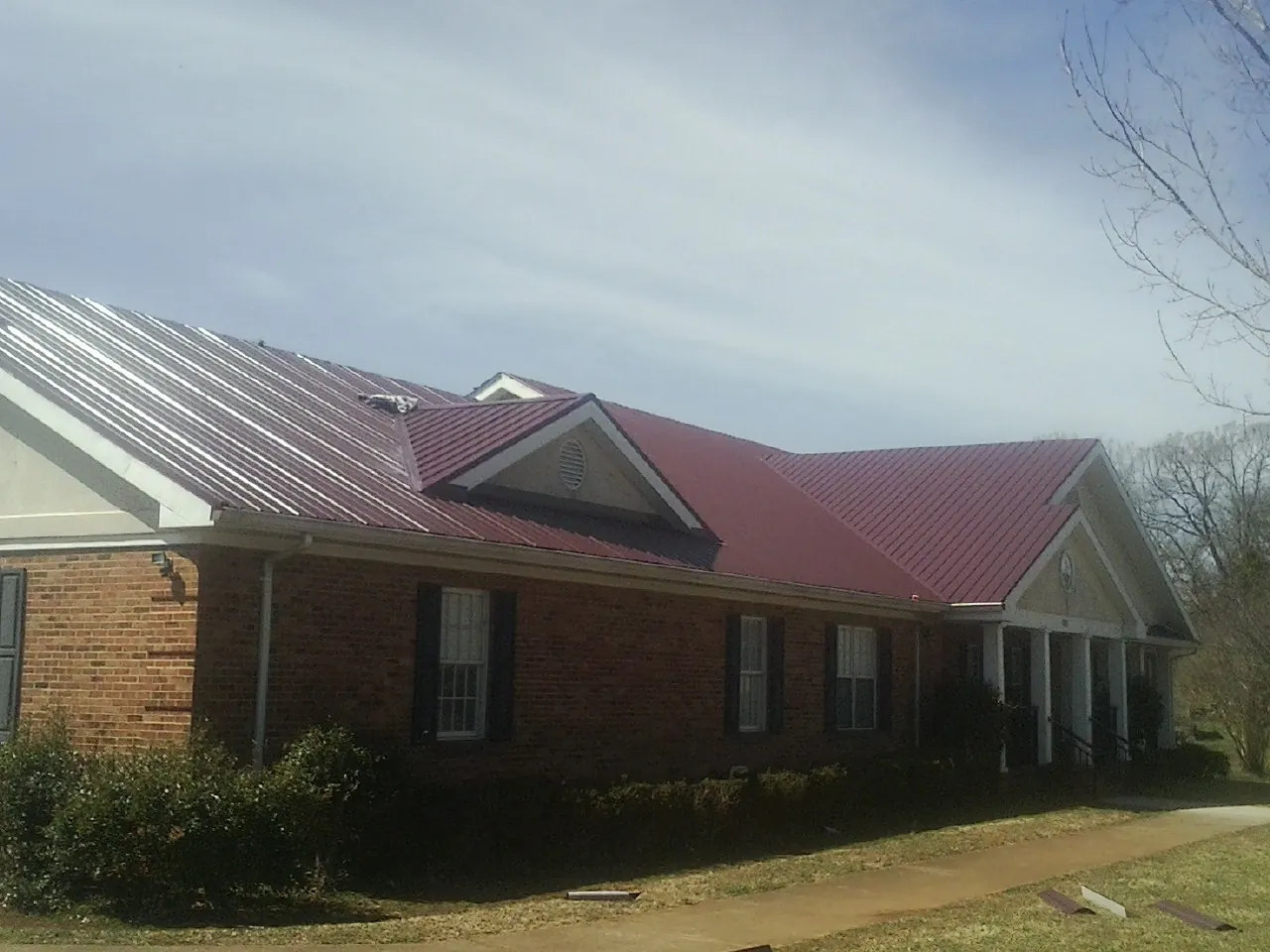 Red metal roof with gabled entries on a long brick building, from a Hail Damage Roof Repair job in Williams