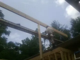 Carpenter setting a ridge beam over a new addition frame in Williams