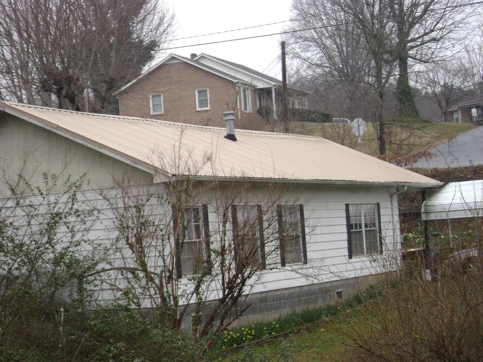 Tan metal roof on a white sided house set into a hillside — Commercial Roofing by Roofing Brothers in Williams